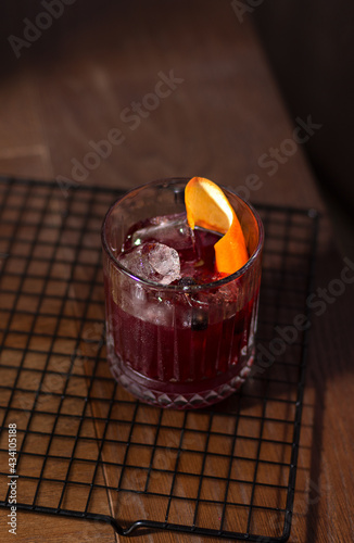 Alcoholic refreshing cocktail with black currants and decorated with orange in a transparent beautiful glass with ice on the table. Summer menu concept.