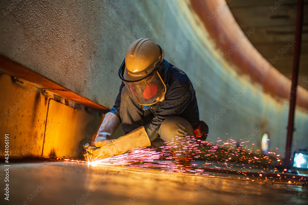 Male worker metal cutting spark on tank bottom steel plate with flash of cutting light close up wear protective gloves and mask Male worker metal cutting spark on tank bottom steel plate with flash of cutting light close up wear protective gloves and mask
