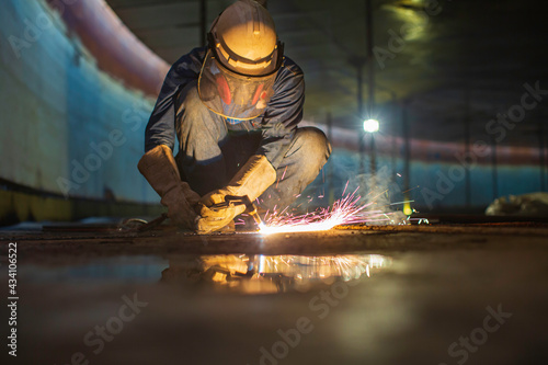 Male worker metal cutting spark on tank bottom steel plate with flash of cutting light close up wear protective gloves and mask