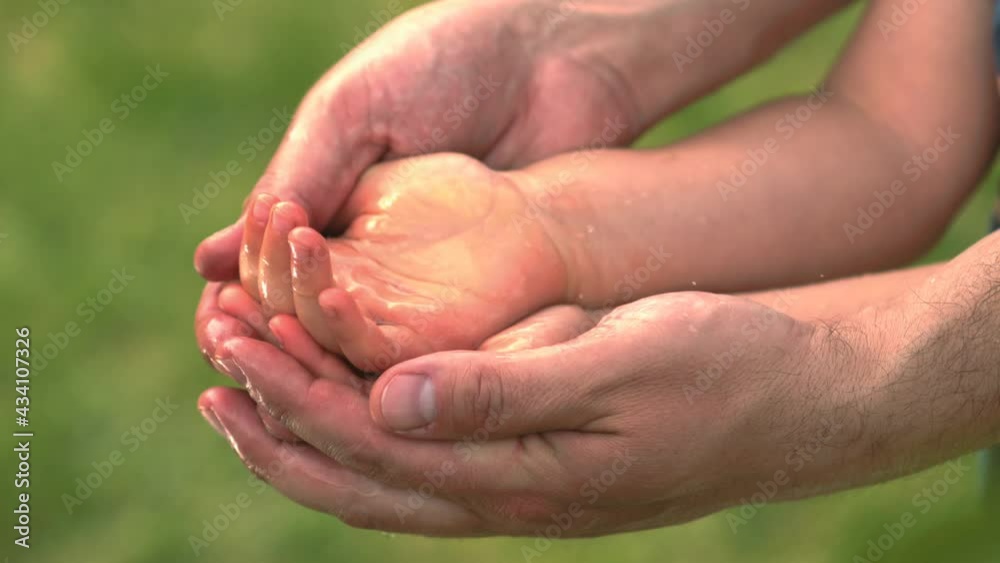 Father Holding Hands of his Child and Water Drops Falling in their Palms in Slow Motion a Concept of Fatherhood Togetherness and Care with Green Leaves on the Background
Father Holding Hands of his Child and Water Drops Falling in their Palms in Slow Motion a Concept of Fatherhood Togetherness and Care with Green Leaves on the Background
