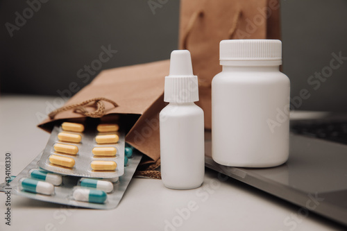 Pills and spray containers and buff paper bags near laptop close-up