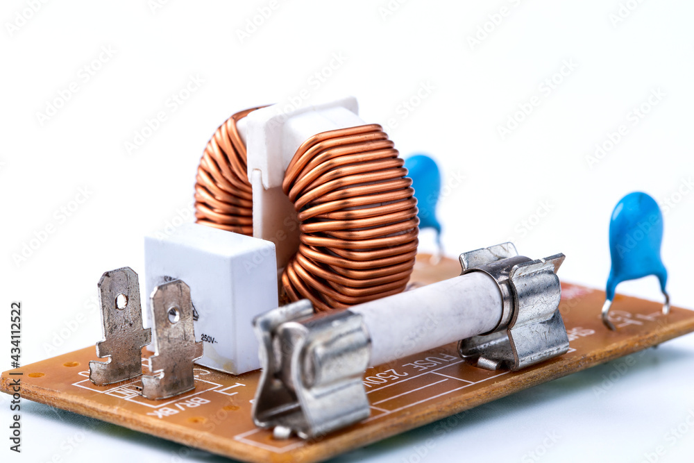 Close up of induction coil with copper wire winding soldered on printed circuit board and electric fuse isolated on white, toroidal inductor. Selective focus. - obrazy, fototapety, plakaty 