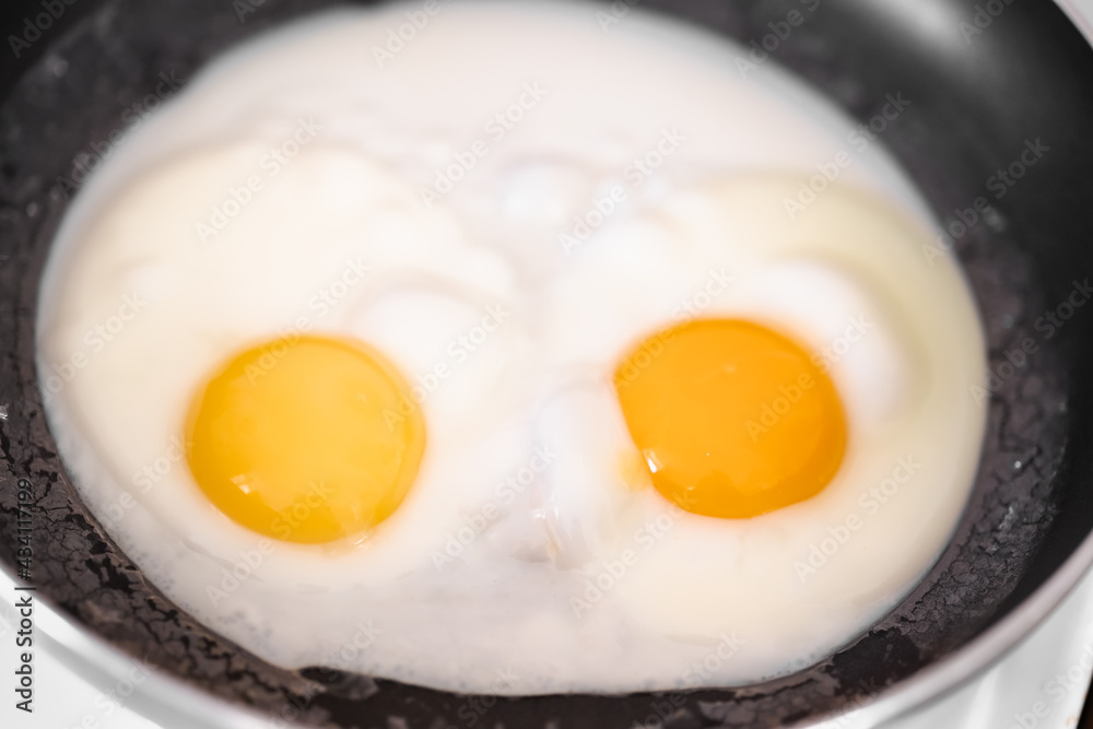 Cooked small fried eggs with two bright round raw yolks in a black skillet. Simple breakfast. Top view, close-up, minimalistic Cooked small fried eggs with two bright round raw yolks in a black skillet. Simple breakfast. Top view, close-up, minimalistic