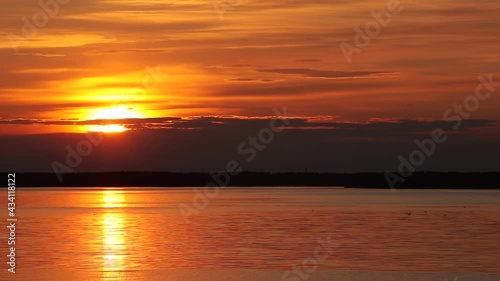 A beautiful sunset over the lake with a golden sun reflecting on the surface with a red and black sky on the horizon and birds flying near the shimmering water