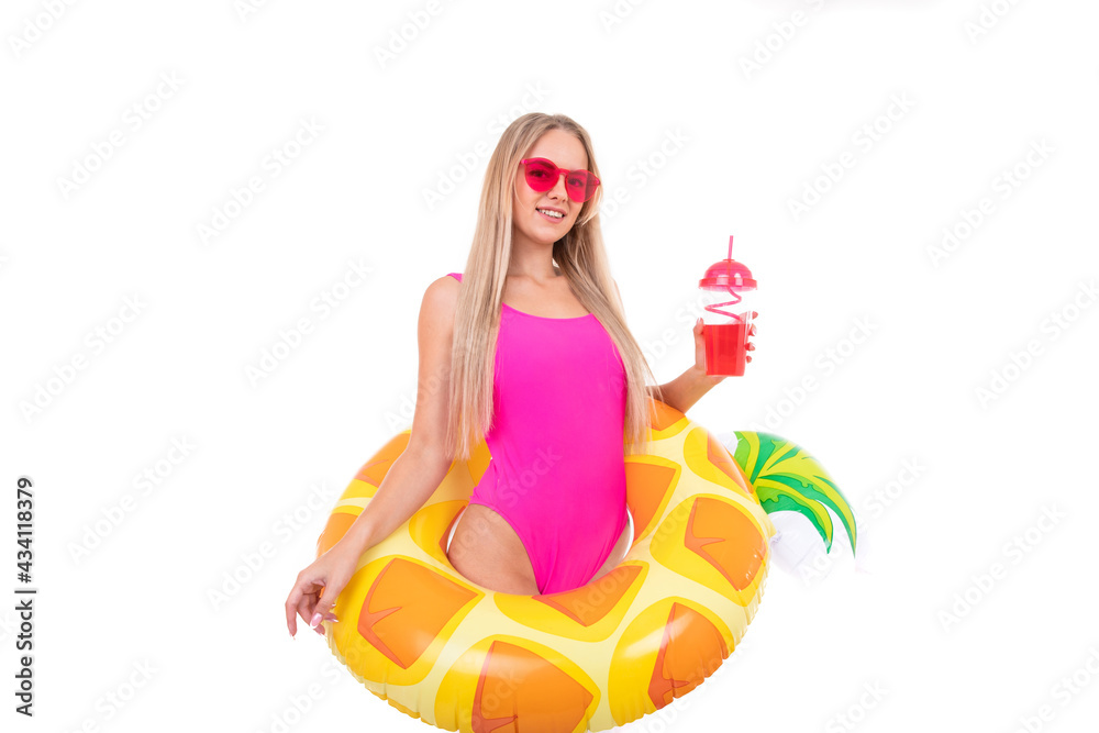 Obraz premium A young woman in a pink swimsuit and glasses holds an inflatable swimming circle and drinks lemonade