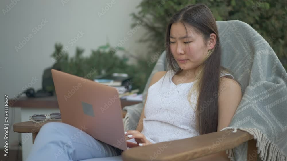 Concentrated professional Asian woman typing on laptop keyboard sitting in home office on deck. Portrait of focused young expert checking e-market. Remote working concept Concentrated professional Asian woman typing on laptop keyboard sitting in home office on deck. Portrait of focused young expert checking e-market. Remote working concept