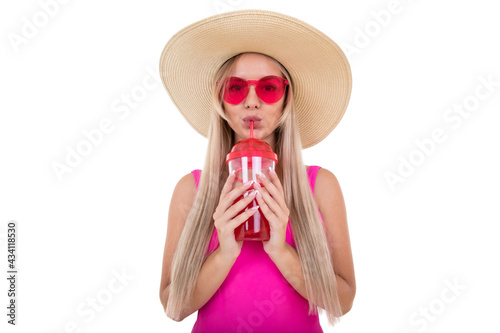 A blonde young woman in a pink bathing suit and hat drinks lemonade