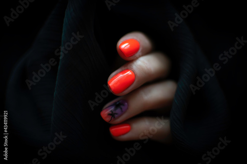 Colorful nail design on black background. Bright orange nail polish with ombre details and hand painted palm trees. Selective focus on a finger, blurred background.