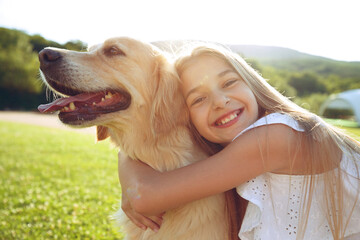 Cute smiling little girl hugs a retriever in a summer park. High quality photo