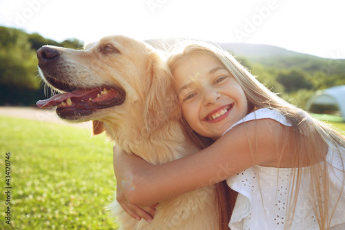 Murais de parede Cute smiling little girl hugs a retriever in a summer park