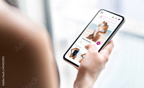 Online shop website in phone. Fashion store product page in smartphone. Woman looking for swimsuit sale. Web site mockup. Ecommerce and retail business concept. Customer buying and ordering apparel.