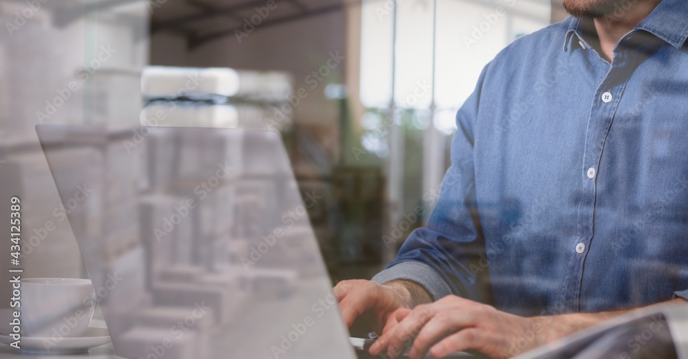 Composition of man using laptop over stacked up shelves with boxes in warehouse