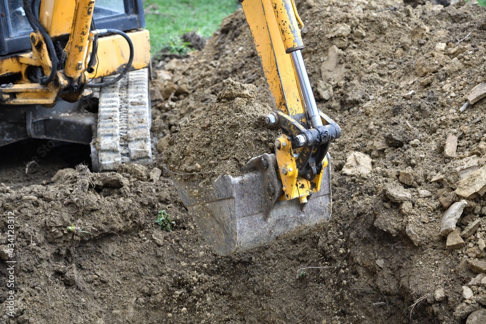 A road excavator dredges the ground foundations near the house