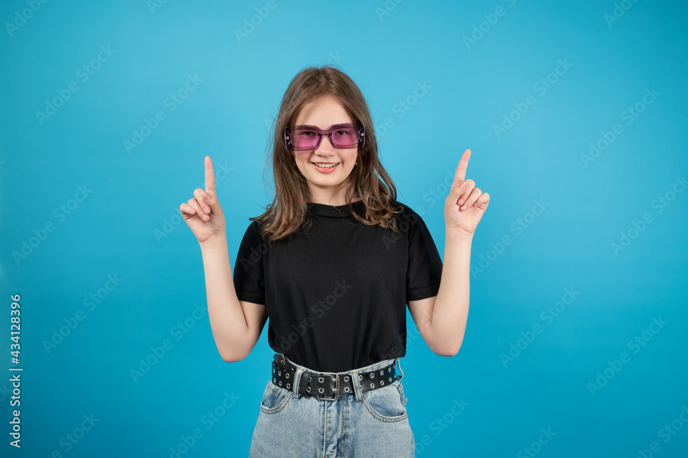 The girl smiles, looks straight and points her hands to the side on blue background The girl smiles, looks straight and points her hands to the side on blue background