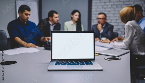 Team of blurred business entrepreneurs communicate at desktop with computer technology with mock up screen for web advertising, experts working at table with modern laptop device with blank screen