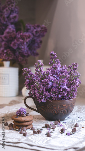 Decorative composition with a Bouquet of lilacs. Clay cup of tea and chocolate cake. A bouquet of lilacs in a vase. Spring floral background with lilacs in the interior. 