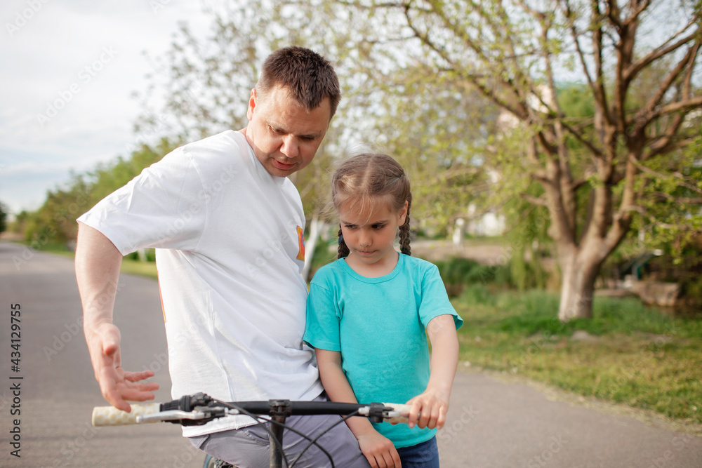 Father teaching her little daughter to ride a bicycle, happy summer in village, healthy lifestyle, childhood, fatherhood and upbringing, concept for father day