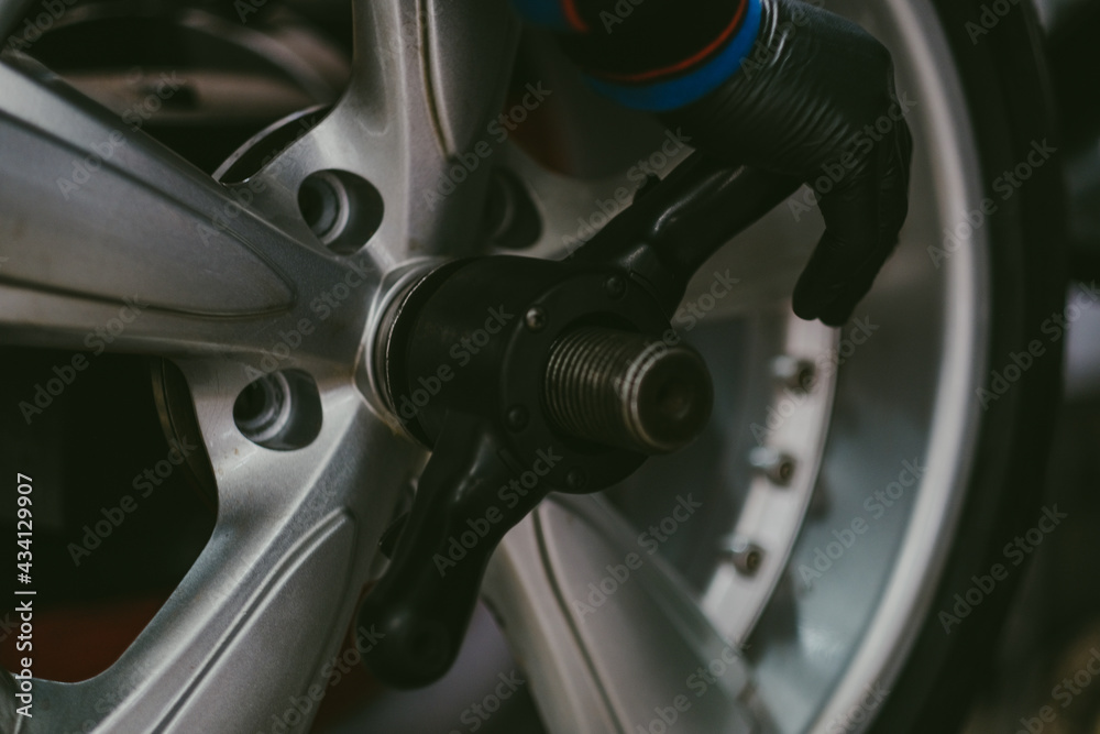 Gloved hand of a mechanic in a workshop removing the rim of a car wheel with a special tool