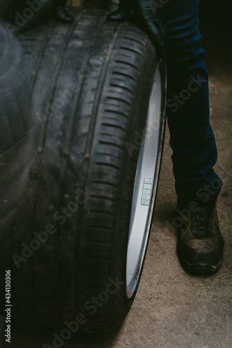 Mechanic in a workshop rolling a large car tire on the ground