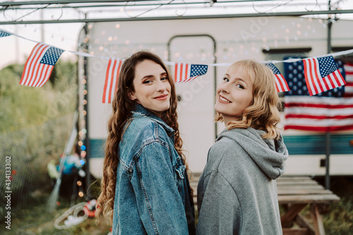 Dos chicas jovenes celebrando día de la independencia de estados unidos con barbacoa frente a una caravana con la bandera americana