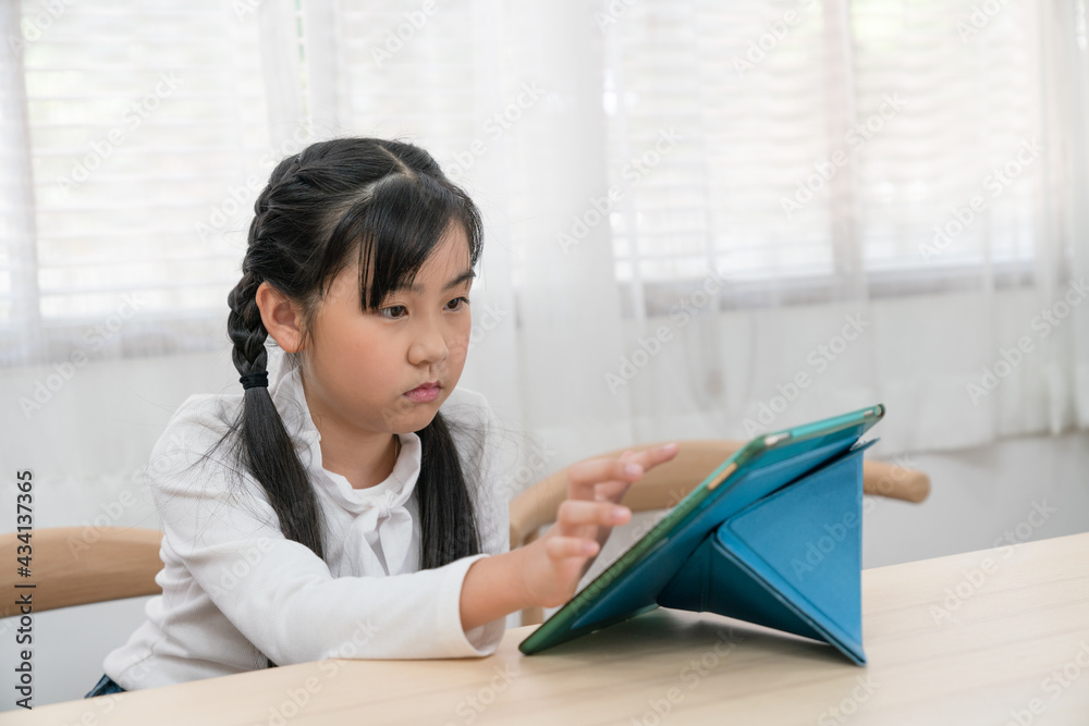 Sad Asian young girl sitting alone playing digital tablet while parents are still working, they don't have time to take care of their daughters. Sad Asian young girl sitting alone playing digital tablet while parents are still working, they don't have time to take care of their daughters.