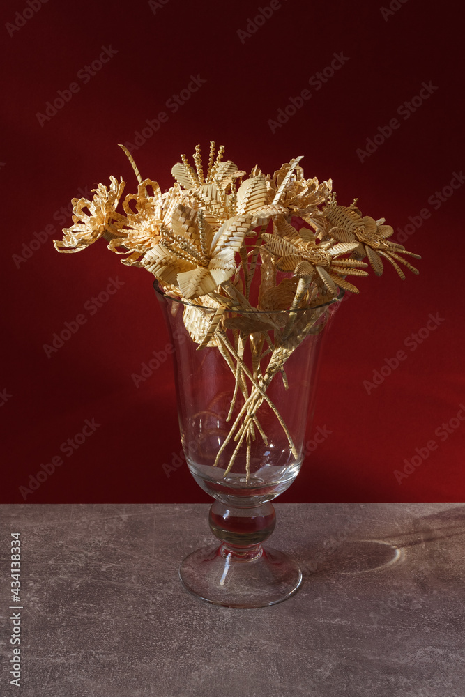 A glass vase with a bouquet of flowers made from straw on a red background. Close-up
