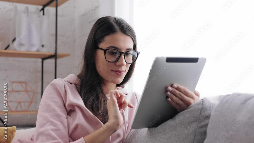 Portrait of Attractive brunette female in glasses using gadget. Technology concept. Joyful Girl using digital tablet at home. smiling young beautiful woman texting on digital tablet in living room. Portrait of Attractive brunette female in glasses using gadget. Technology concept. Joyful Girl using digital tablet at home. smiling young beautiful woman texting on digital tablet in living room.