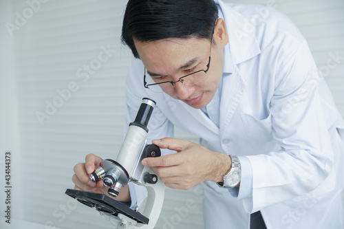 Close up of Asian Scientist man with white coat and glasses using microscope for experiment and research at laboratory. white background