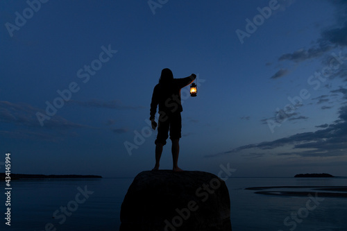 Man standing on the rock and holding old lantern outdoors near the sea at night.  Light and hope concept.
