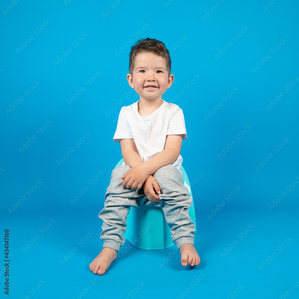 Happy toddler boy sitting on a plastic potty, blue background with copy space.