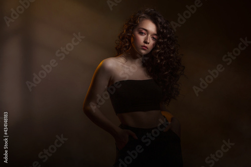 Beauty young woman with curly big and long hair. Glamour lady on dark background. Cute woman face wavy hair, perfect make up, red lips