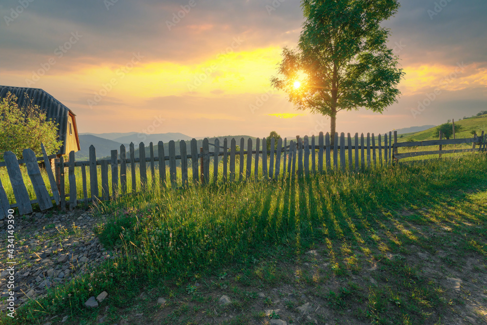 Obraz premium Beautiful scenery view from the mountain village street. Rural road with wooden fence and long shadows from its planks of the sunlight.