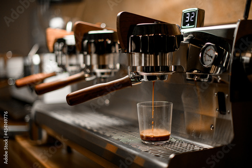 professional coffee machine automatically prepares and pours espresso drink into clear glass © fesenko
