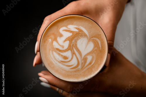 top view of glass with coffee drink in hands of woman. Beautiful pattern on foam