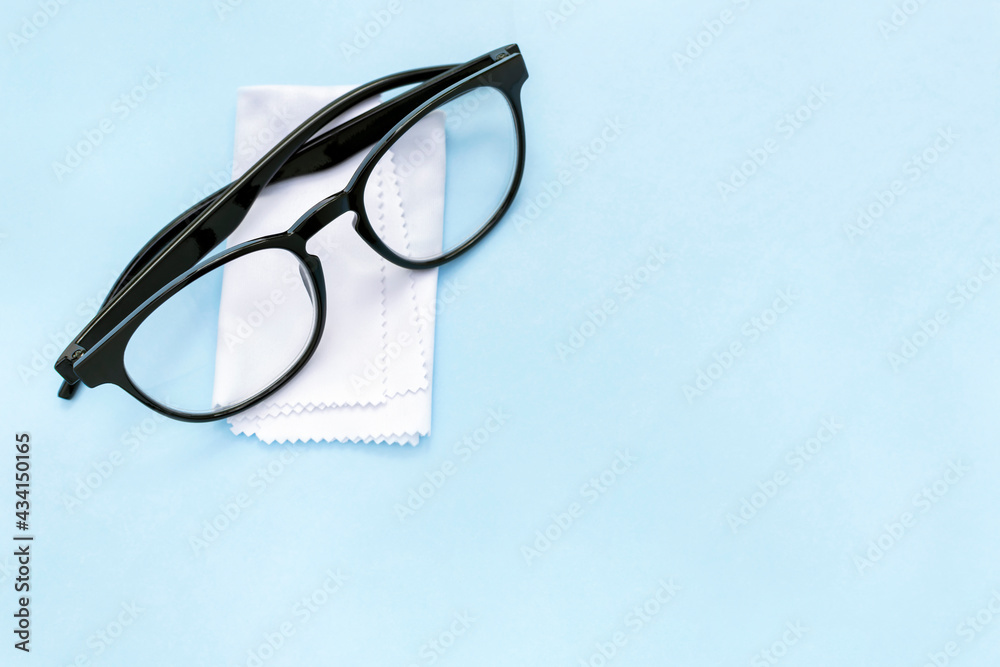 Black rimmed glasses and cleaning cloth on blue background with copy