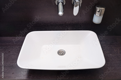 White bathroom sink on an black wooden countertop with a soap dispenser