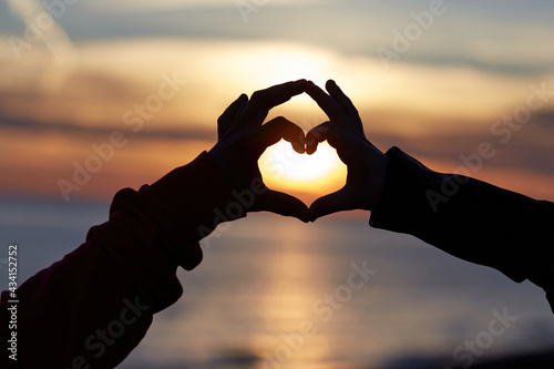 Heart shape with hands of loving couple on sunset sky background photo