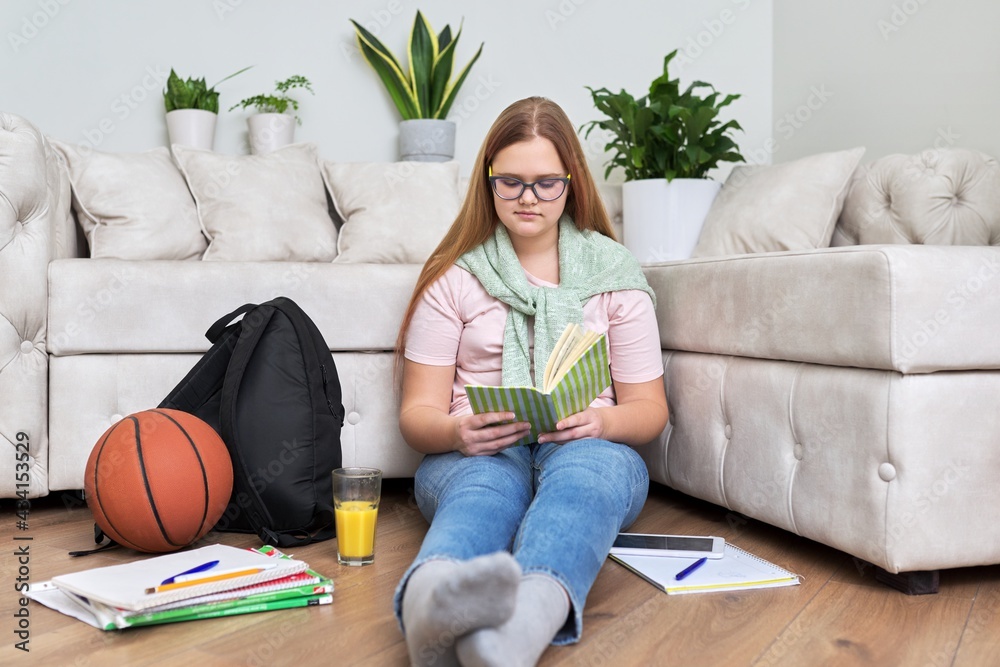 Teenage girl sitting at home on the living room floor reading book Teenage girl sitting at home on the living room floor reading book
