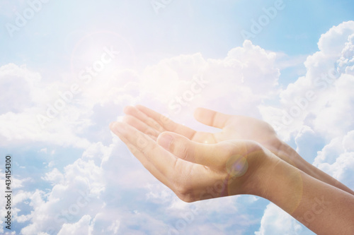 A woman raises her hands up to the sky over a white large cloud to pray and worship God. Freedom concept or Christian prayer background