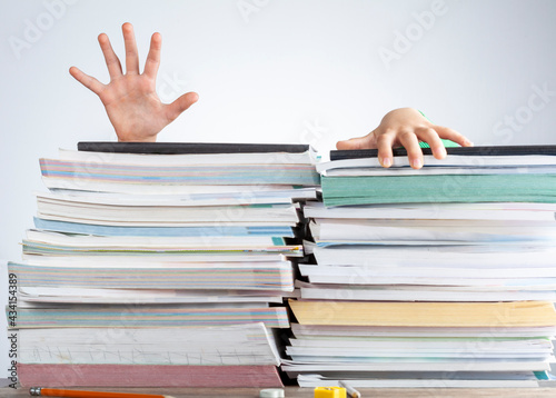 фотографія Abstract concept image showing a young student behind a large pile of test prep books on a study desk