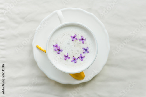 Mug of cappuccino on a beige background. Lilac flowers. Rest at home. Quarantine.