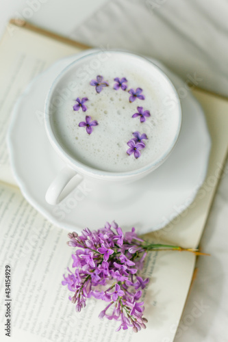 Mug of cappuccino on a beige background. Lilac flowers  book. Rest at home. Quarantine.