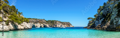 Panoramic view from an empty Cala Macarelleta, with turquoise waters and blue sky, in Menorca, Balearic Islands, Spain