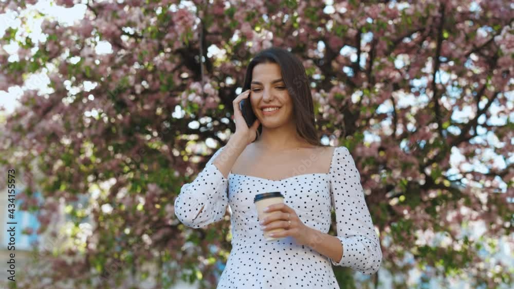 Portrait of girl walking with mobile phone and paper coffee cup. Beautiful woman talking phone with takeaway coffee in hands on street. Cheerful woman relaxing with cellphone and hot drink outdoors Portrait of girl walking with mobile phone and paper coffee cup. Beautiful woman talking phone with takeaway coffee in hands on street. Cheerful woman relaxing with cellphone and hot drink outdoors