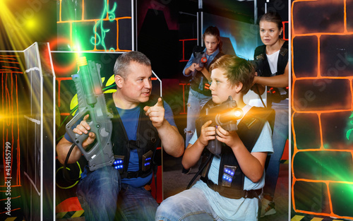 Happy glad cheerful positive smiling teen boy with laser gun having fun on lasertag arena with his father