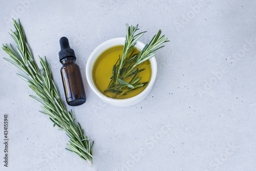 Bottle of essential oil with fresh rosemary twigs on a light surface