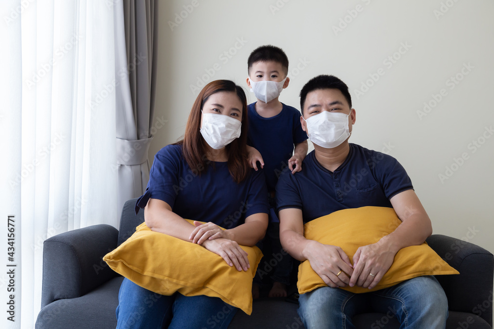 Asian family wearing protective medical mask for prevent virus Covid-19 and sitting together in living room. Family protection from contaminated air concept