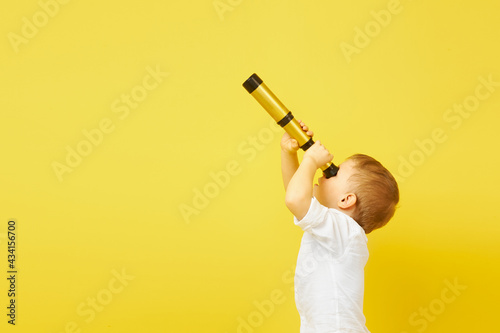 Side view of a child looking through a telescope on a yellow background. The concept of travel, pirates and adventures, active lifestyle, striving for the goal photo
