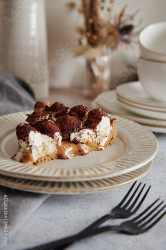 Vertical shot of delicious Bonafi Cream Pie slice with chocolate powder on a white plate with forks photo