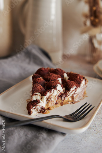 Vertical shot of delicious Bonafi Cream Pie slice with chocolate powder on a white plate with a fork photo